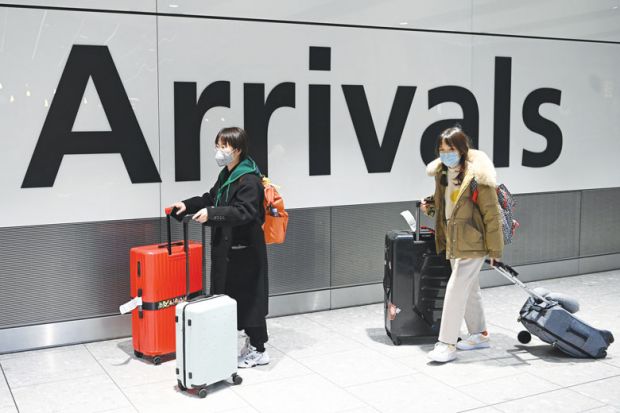 Chinese passengers wear face masks as the push their luggage after arriving from a flight at Terminal 5 of London Heathrow Airport 