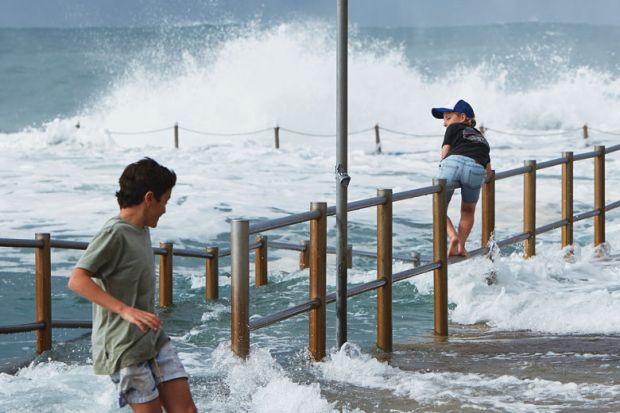 Two boys are seen avoiding large waves washing through the closed ocean pool at Dee Why Point, Sydney, Australia 