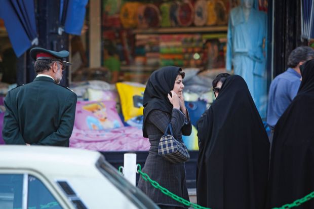 An Iranian woman adjusts her scarf as two veiled morality policewomen talk to them in Tehran to illustrate Iranian scholar who resigned in protest may need to seek asylum