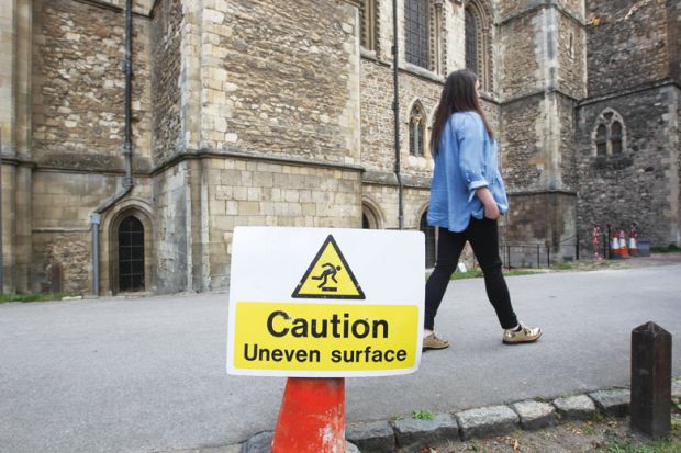 A caution uneven surface is seen while a woman walks past as a metaphor fo, Experts urge caution on positive UK study visa data