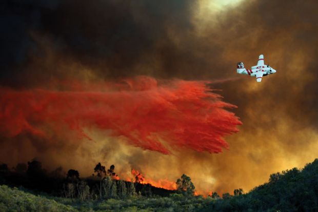 An airplane makes a fire retardant drop on a large hill-top home
