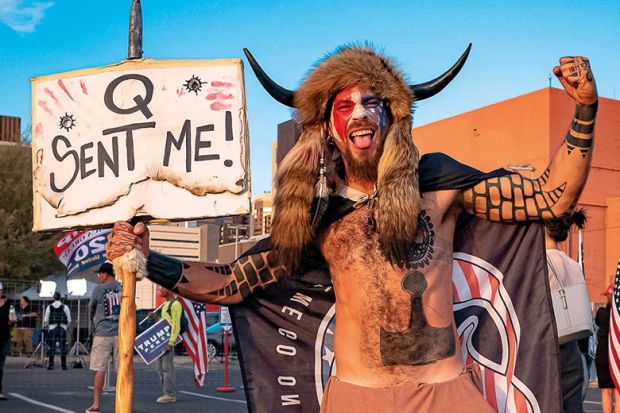 Jake Angeli, 33, aka Yellowstone Wolf, from Phoenix, holds a QAnon sign, as he presents himself as a shamanist and consultant for the Trump supporters gathered in front of the Maricopa County Election Department where ballots are counted after the US pres