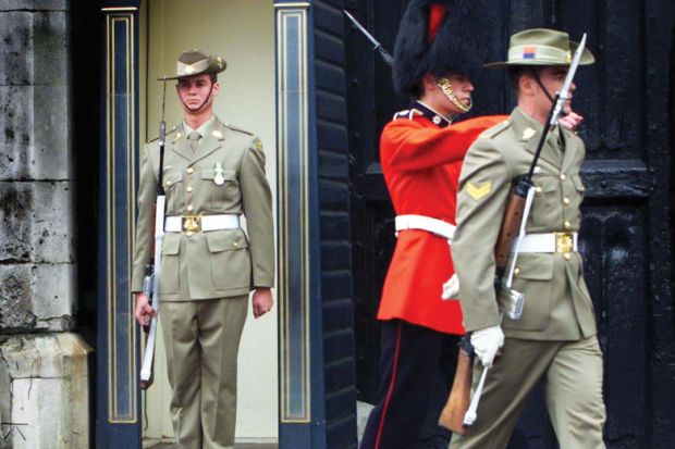 A member of Australia's Federation Guard mans the sentry box with two other guards marching away, one also an Australia's Federation Guard the other a British Grenadier Guard, as a metaphor for Australian institutions changing guard.