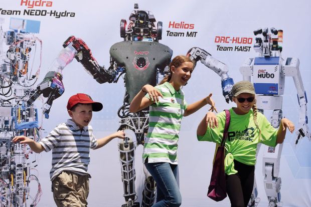 Children pose in front of a promotional poster during the finals of the DARPA Robotics Challenge to illustrate Canada joining the rush to create a Darpa