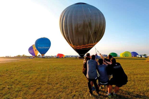 People pull on a rope to lift their hot-air balloon to illustrate Few UK universities raise overseas fees in line with inflation