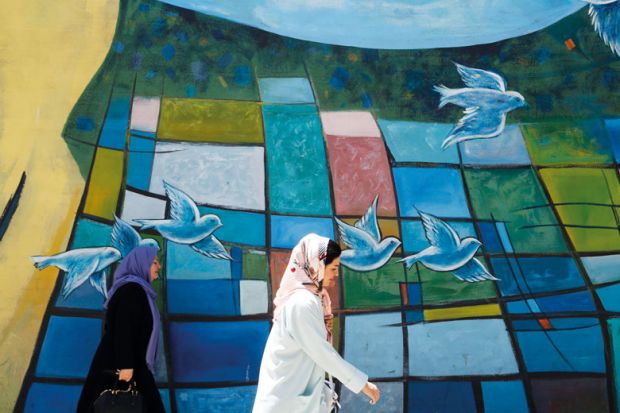 Iranian women walk past graffiti of birds flying in downtown Tehran to illustrate Scholars see politics behind Iran’s India branch campus move