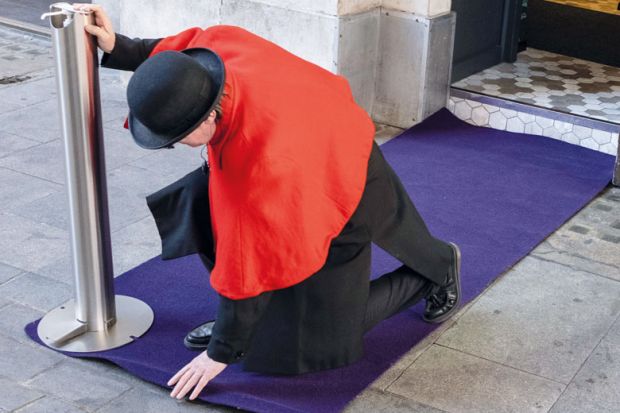 Person in bowler hat  flattens a doorway carpet before an event for special guests to illustrate 'finding a new v-c brings hug responsibility'