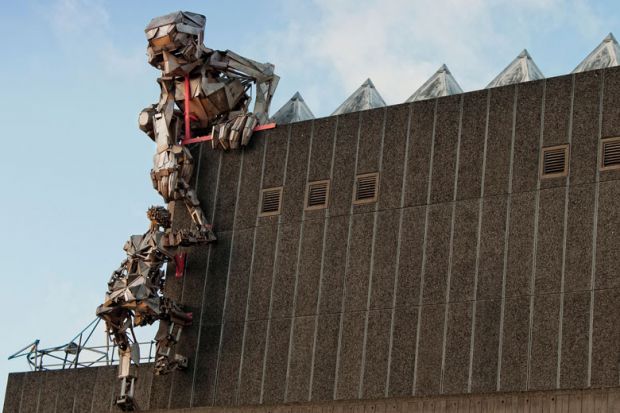 Robot sculptures climbing up the Hayward Gallery, London to illustrate Germany’s largest university buys UK college and degree powers