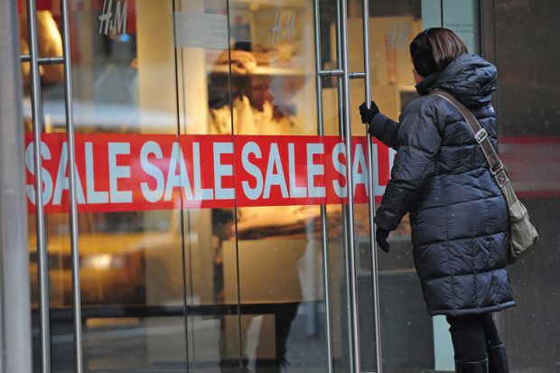 A woman enters a shop displaying a sale sign for Smaller US colleges try big fee cuts to tempt students back