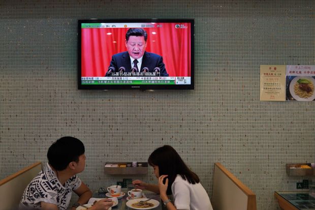  couple eat lunch in a cafe in Hong Kong under a television showing China's President Xi Jinping giving a speech to illustrate Changing of guard in Hong Kong leadership ‘may narrow diversity’