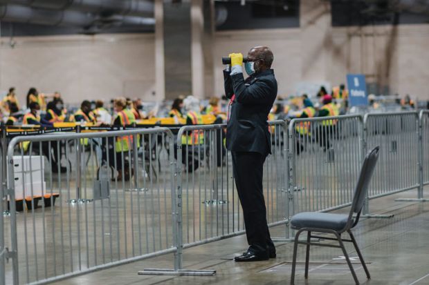 An official poll watcher uses binoculars as workers count ballots for the 2020 Presidential election.