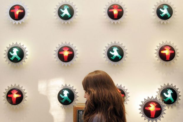 Person walking past a wall with an number of little traffic lights of red and green man in the centre of each as a metaphor for confused communication