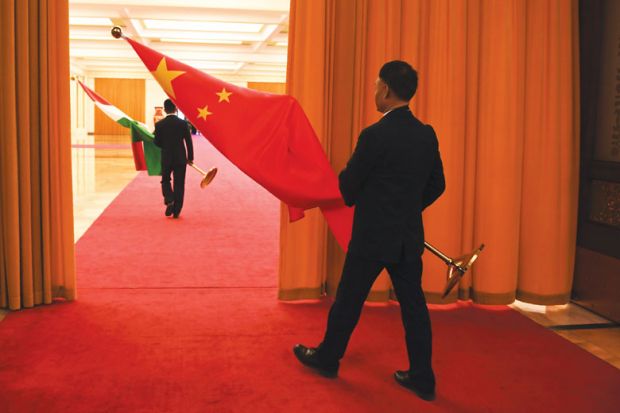 An attendant carries a Chinese flag on to a stage with another attendant in front carrying a Hungarian flag as a metaphor for the Chinese campus being built in Hungary.
