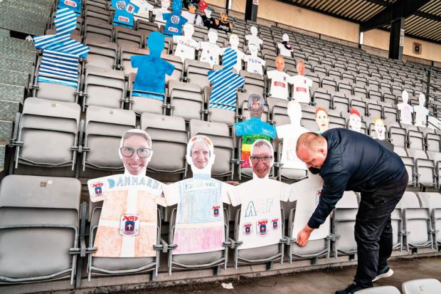 A man places cardboard figures with pictures of the fans in the empty tribunes of the Ceres Park Football Stadium