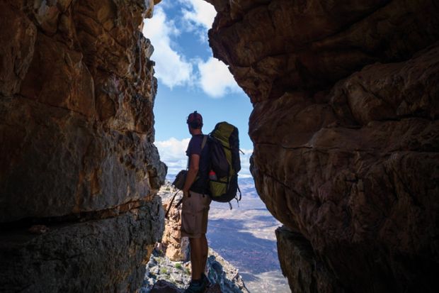 Hiker observes view from gap in rocks