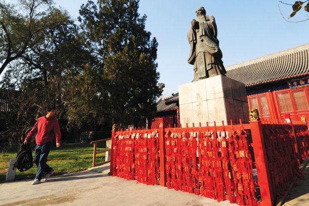 A man walking past looks at a statue of Chinese philosopher Confucius