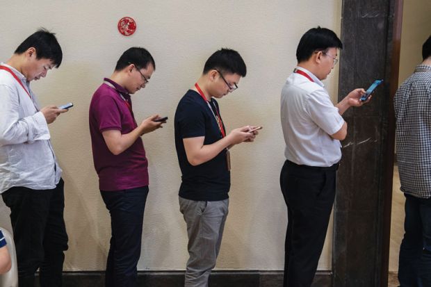 row of men  look at their smartphones 