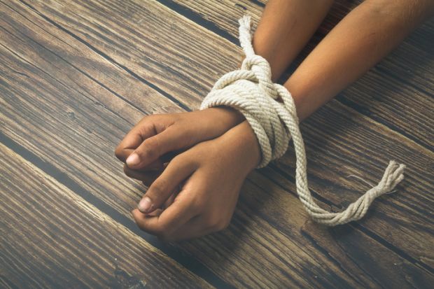 A person's wrists bound with a rope, symbolising the restriction of academic freedom