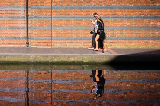 Young couple walking along canal with reflection on water