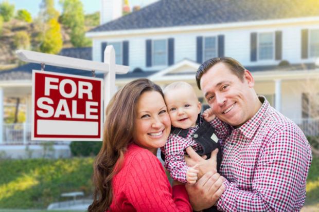 Young couple with baby next to house for sale sign