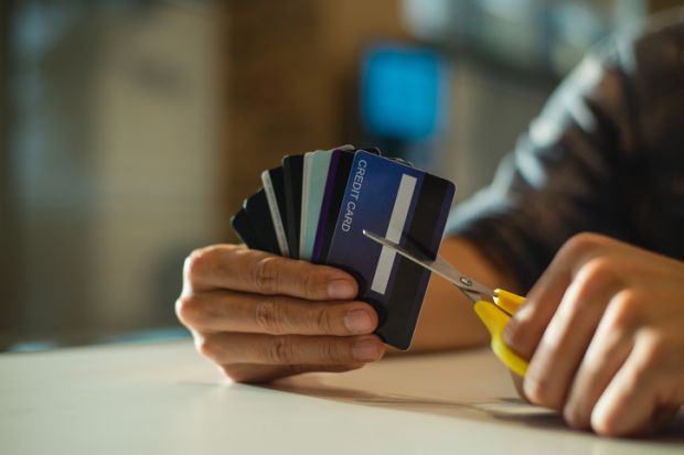 Young man cutting credit card with scissors