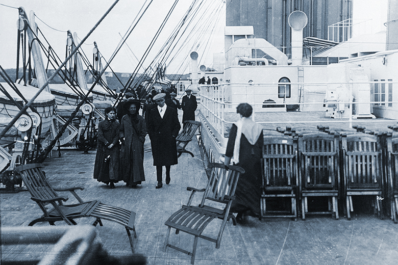 Passengers stroll past neatly arranged deckchairs on the deck of the Titanic, with added deckchairs. 