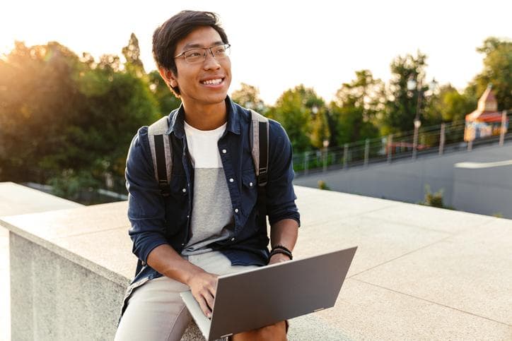 Male student studying with a laptop outside