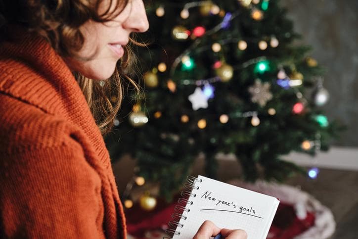 woman writing new years goals on a notepad in front of a christmas tree