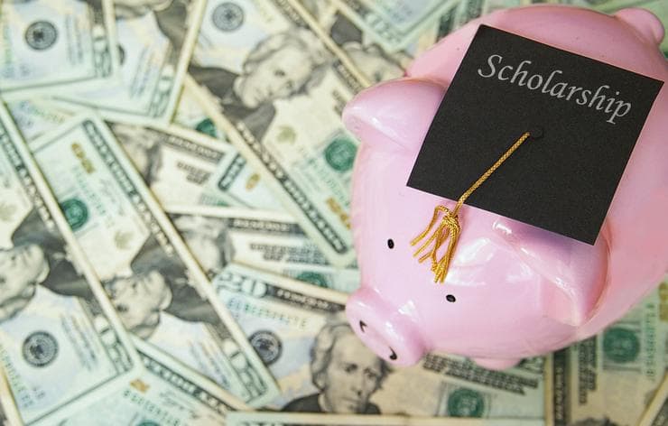 Scholarship graduation hat on a piggy bank surrounded by dollar notes