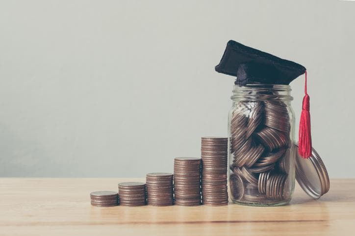 Coins in jar with money stack next to it and a university cap on top