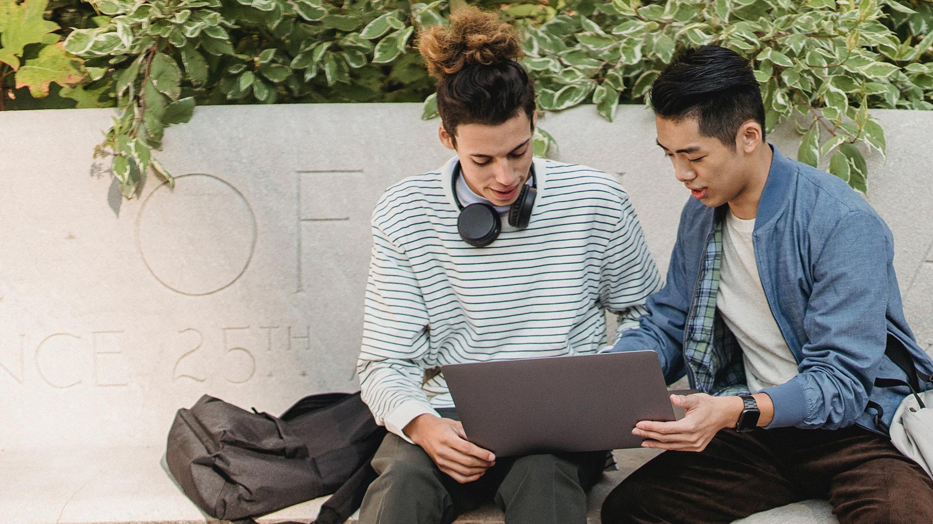 Two students seated outside looking at a laptop