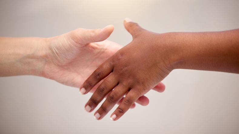 Shot of two hands reaching for one another with different skin tones