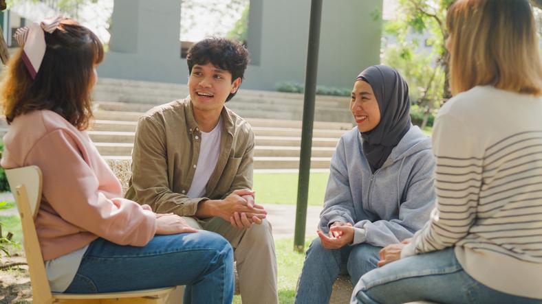 Small group of young people sit in a close circle smiling / iStock