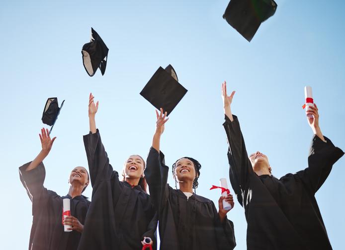 Graduation, students and education goal success celebration with happy women excited victory hat throw/iStock