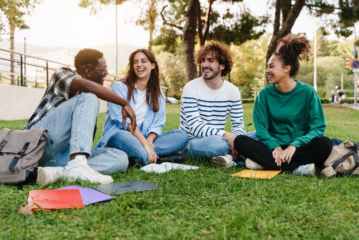 University student friends sitting on the grass, talking in the college campus/iStock