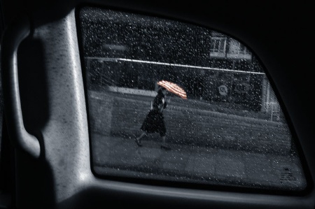 Woman walking in rain with umbrella, viewed through taxi window