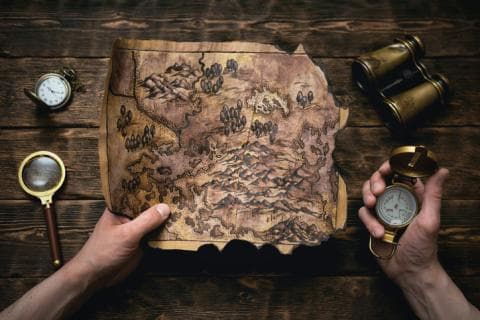 A treasure map, compass and binoculars are laid out on a table