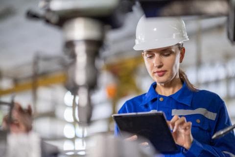 An engineer controls the quality using a tablet device to inspect the drilling machine in the factory
